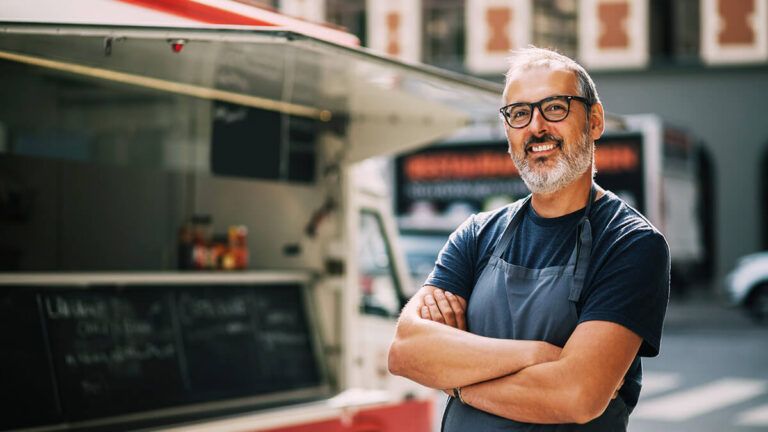 Self-employed man smiling in front of his food truck.