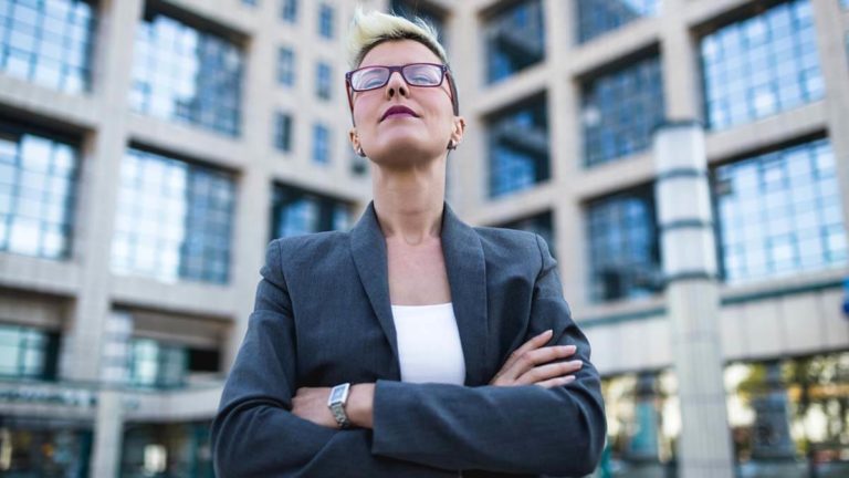 Woman standing in front of corporation with her arms crossed.