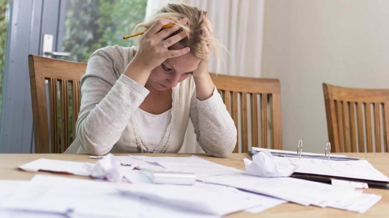 Stressed woman at kitchen table with her hands on her head.