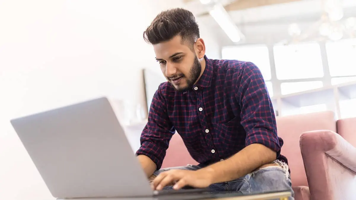 Man sitting on a pink couch working on a laptop.