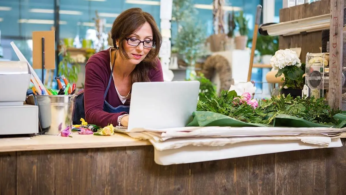 Flower shop owner calculating nontaxable wages on laptop.