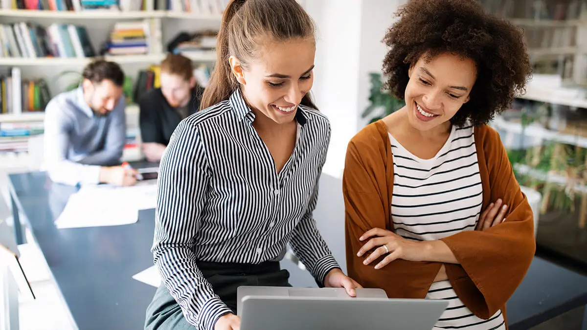 Two women smiling at a laptop.