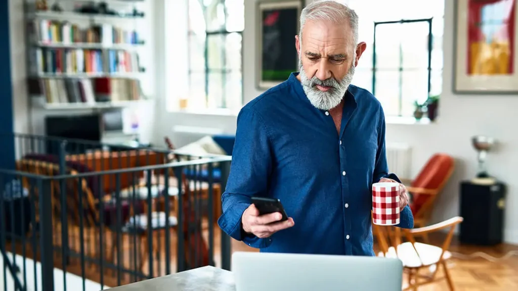 Man looking at his phone and holding a cup of coffee