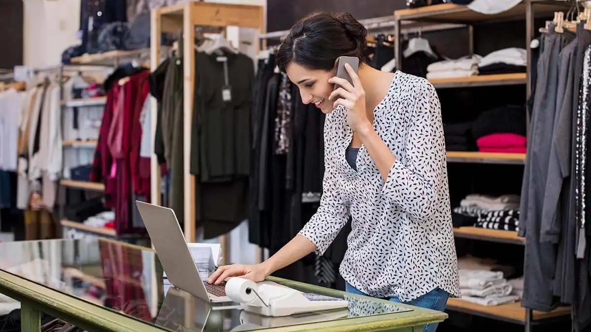 Woman on the phone while looking at laptop.