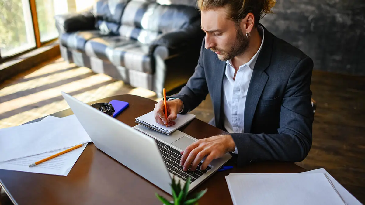 Man writing on notepad and using laptop