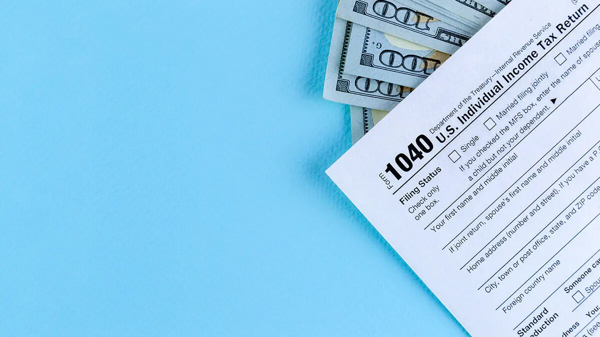 Form 1040 on a blue background with a few $100 bills.