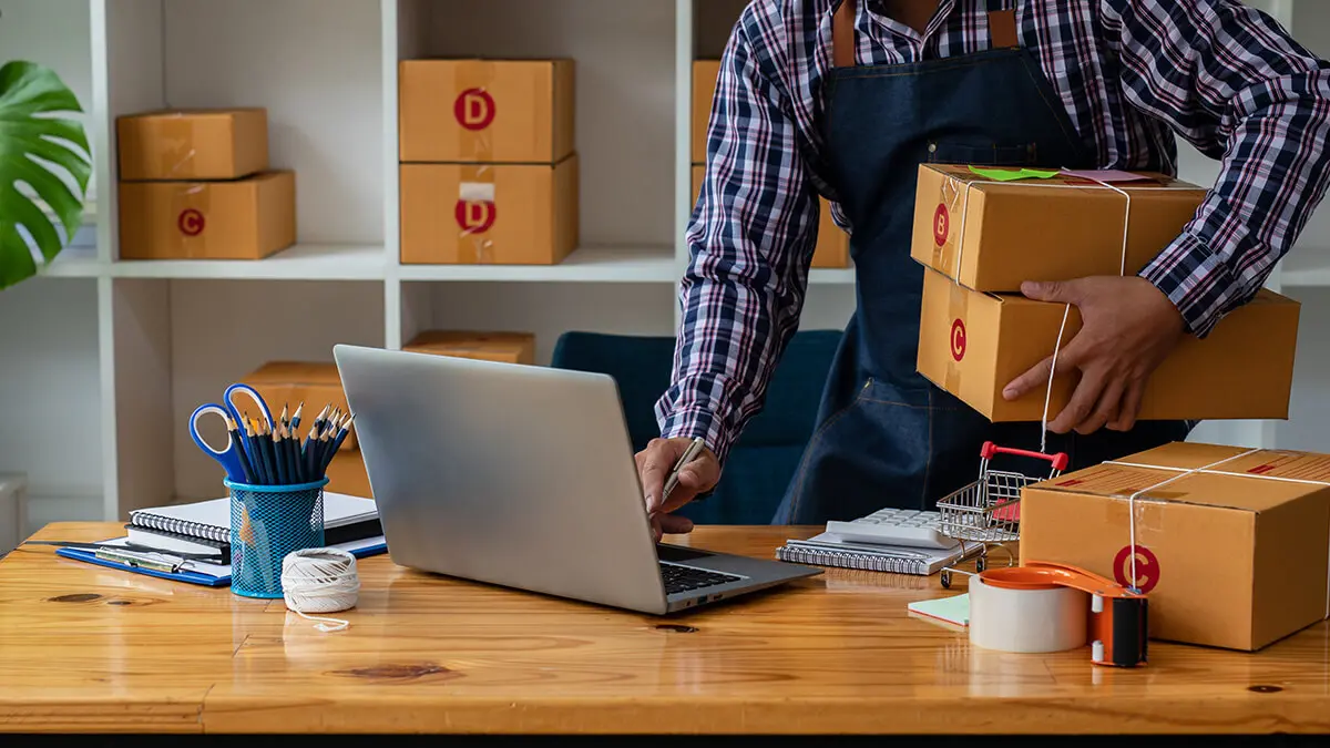 Business owner using the computer in one hand and holding boxes in another