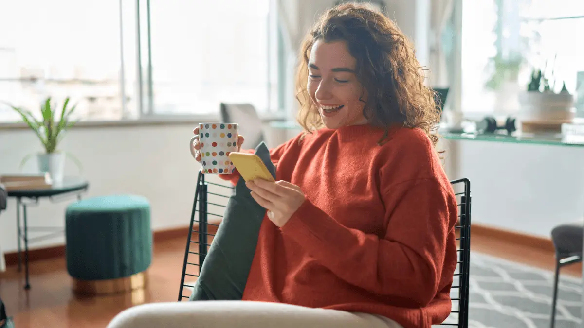 woman looking at funny accounting jokes on her cell phone while drinking coffee